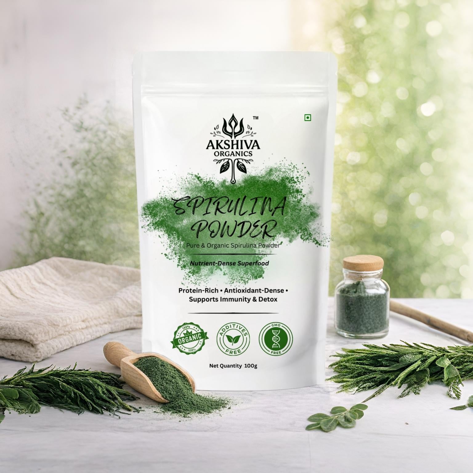 Akshiva Organics Spirulina Powder having premium packaging with green powder, scoop, and herbs on a light background